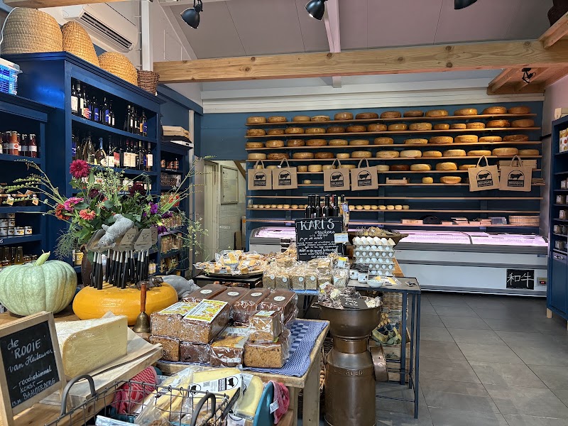 De winkel van binnen: blauwe stellingen, een wand met kaaswielen, streekproducten en bloemen.